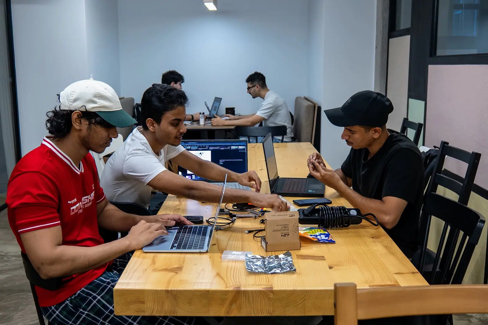 Members at another table working on laptops and hardware